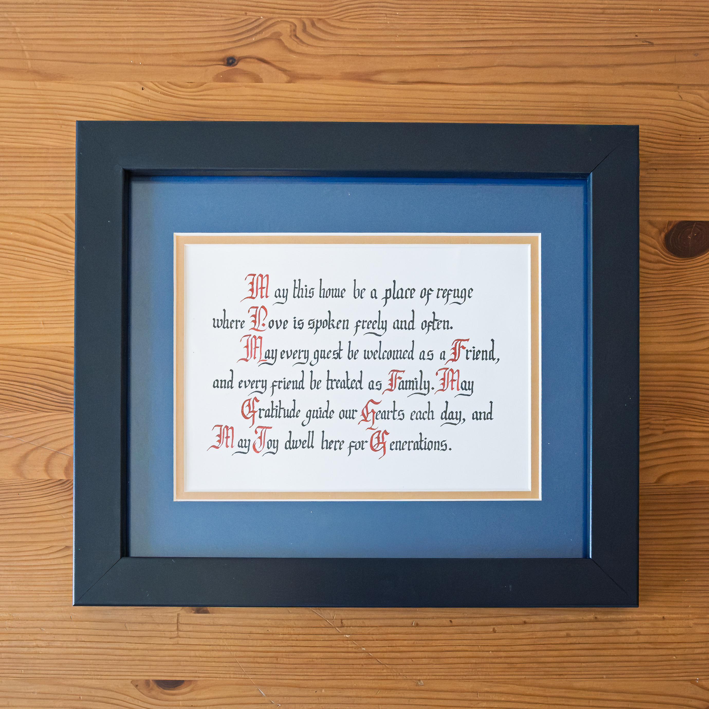 Family blessing calligraphy on ivory paper with red initials beside a candle and ink bottle