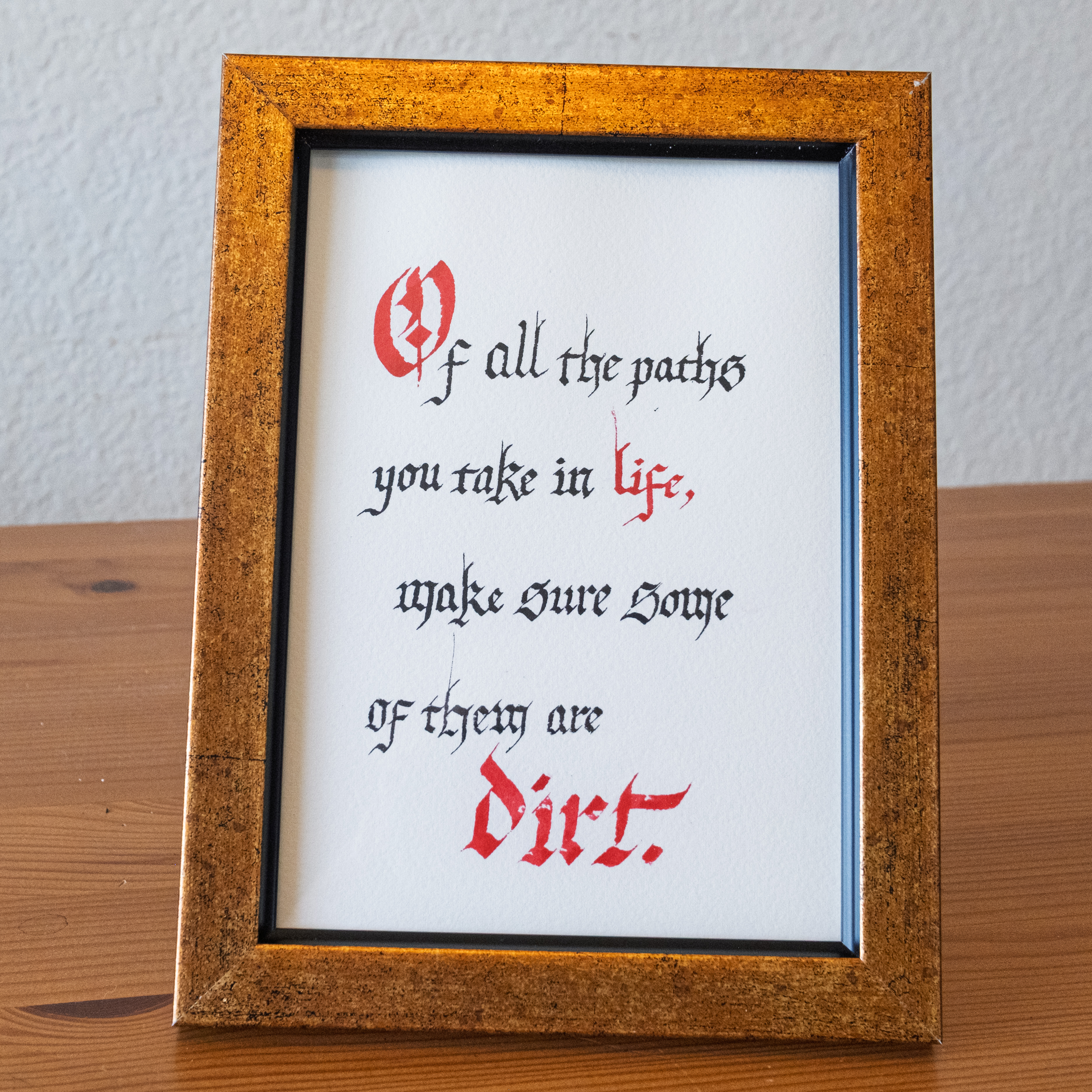 Framed blackletter quote reading Of all the paths you take in life, make sure some of them are dirt