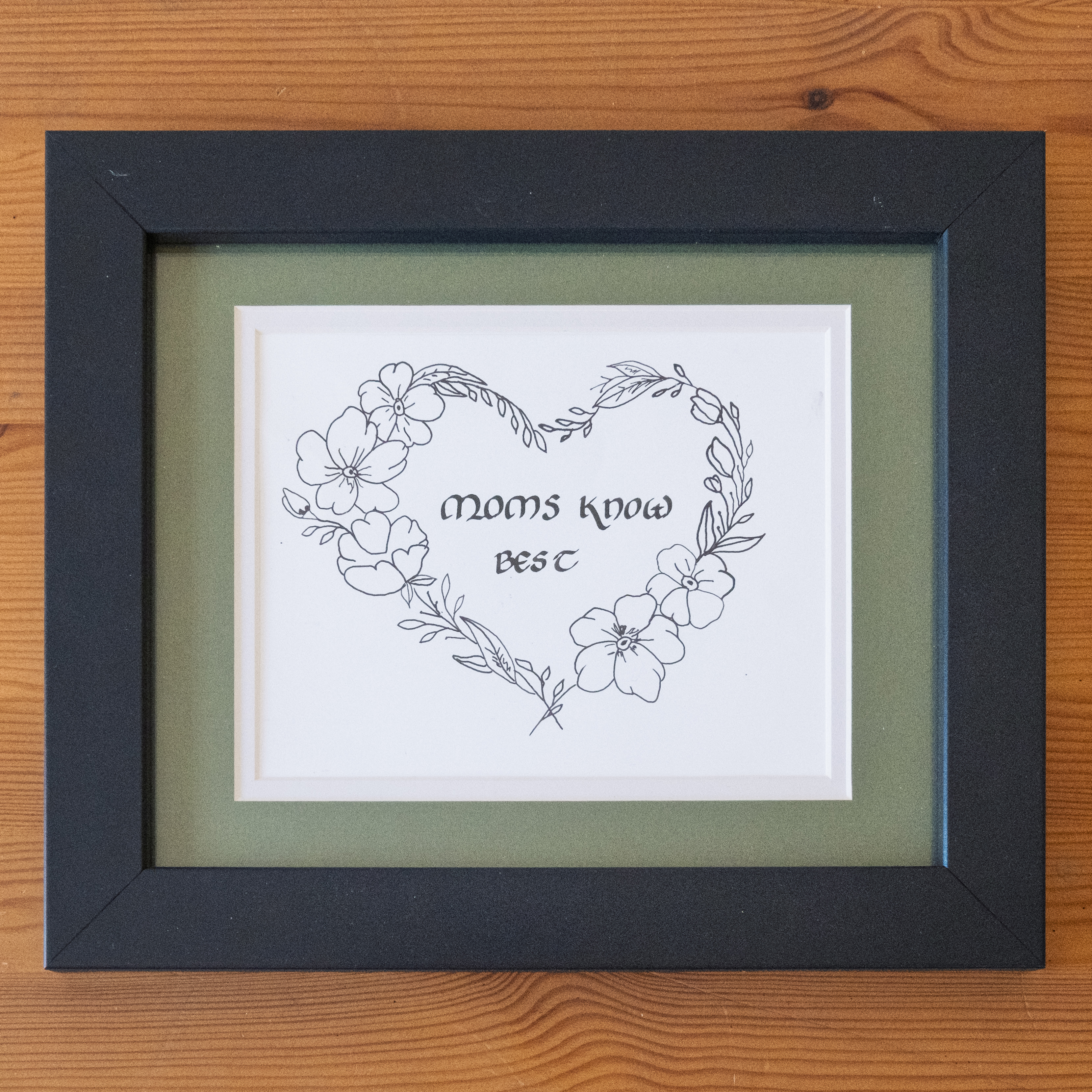 Moms know best calligraphy inside a hand-drawn floral heart border in a green mat and black frame